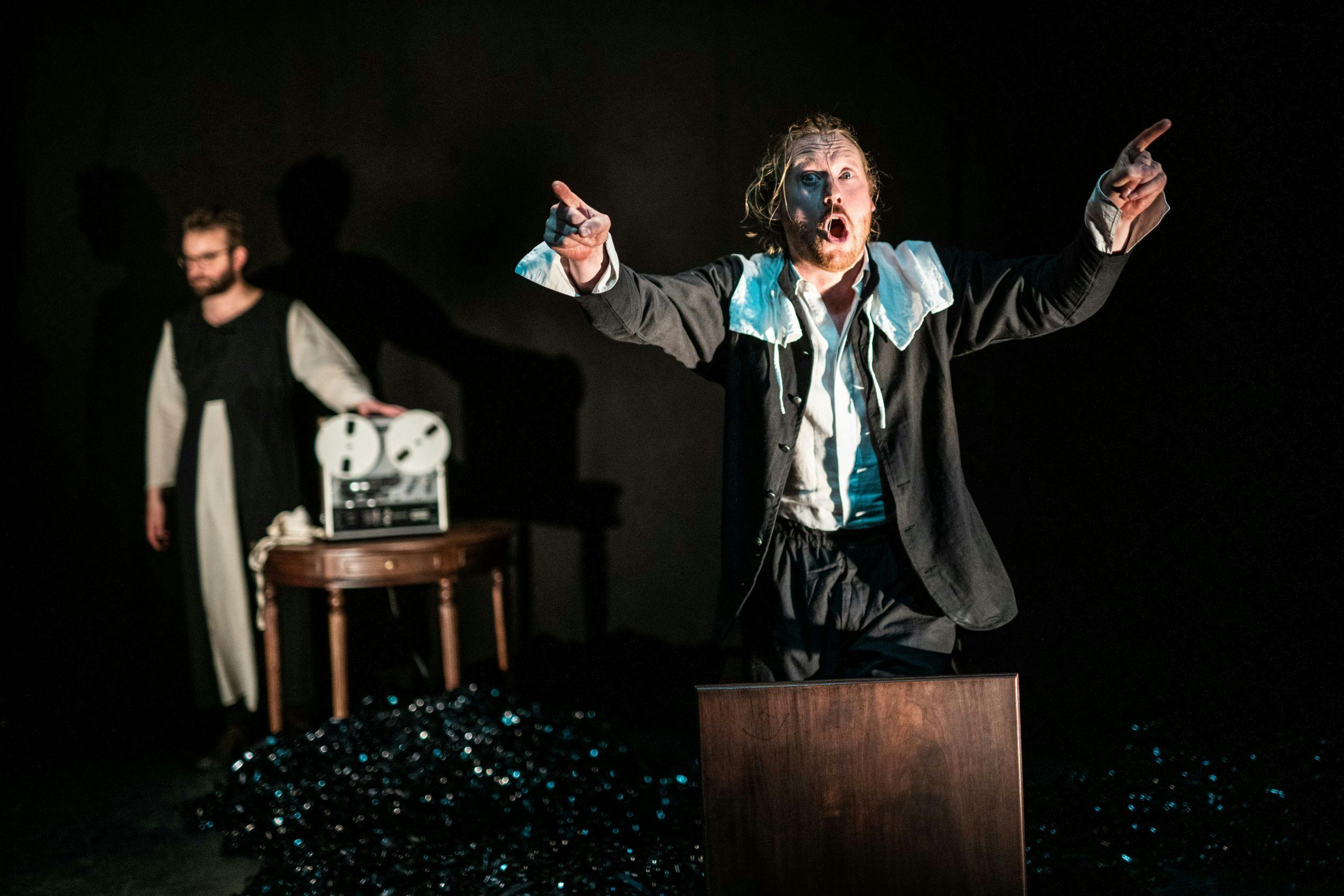 We zien theatermaker Jasper van der Pijl in zijn voorstelling Het Onbenoembare, gekleed in het zwart roept hij met twee handen omhoog naar het publiek.