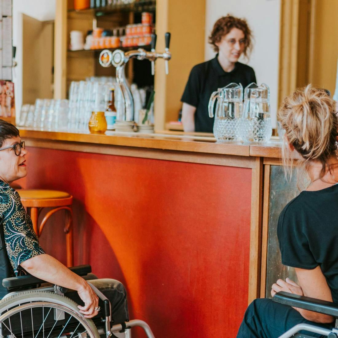 Foto van twee personen in een rolstoel bij de bar